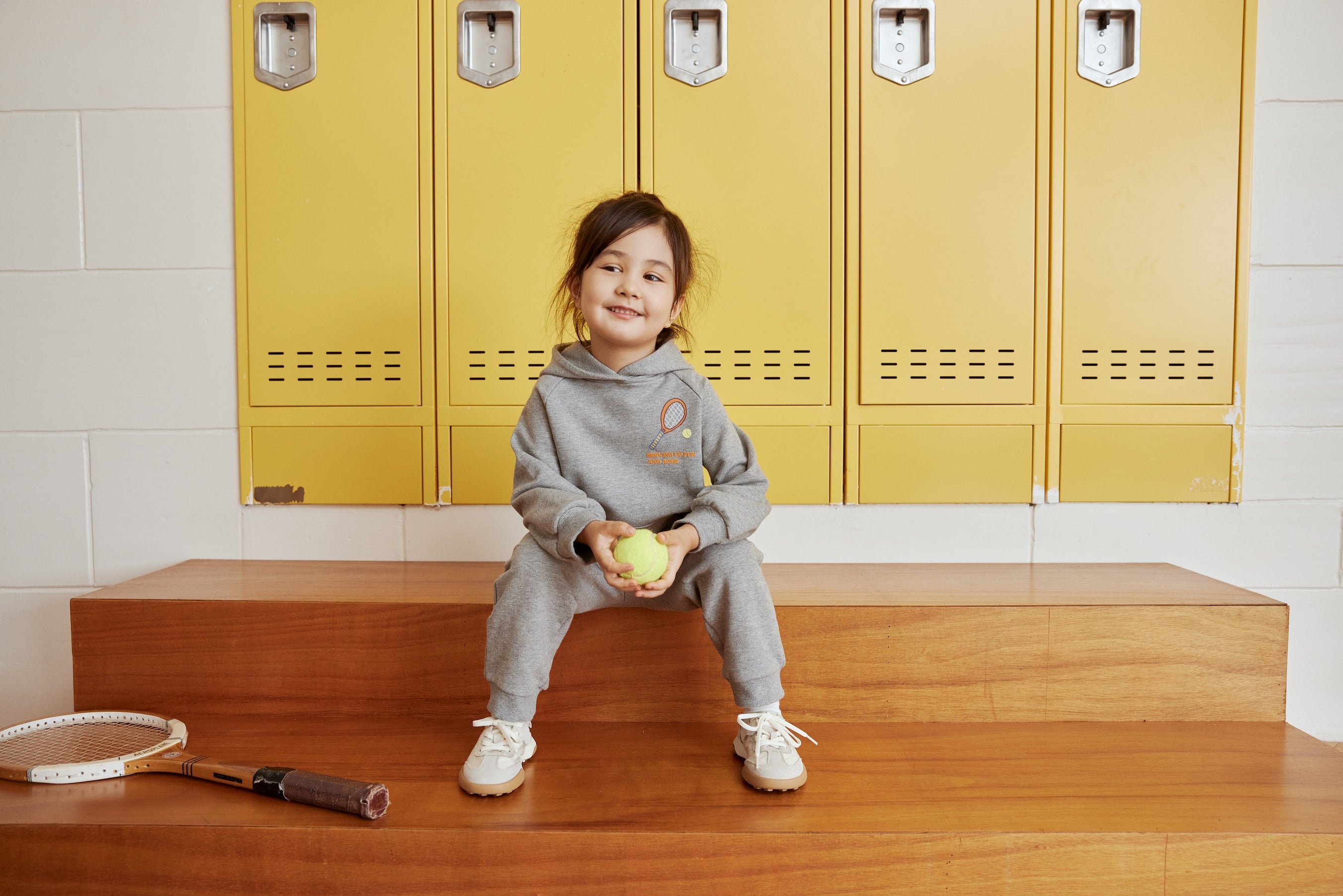 a gril in grey outfit sitting on the bench with a racquet beside her