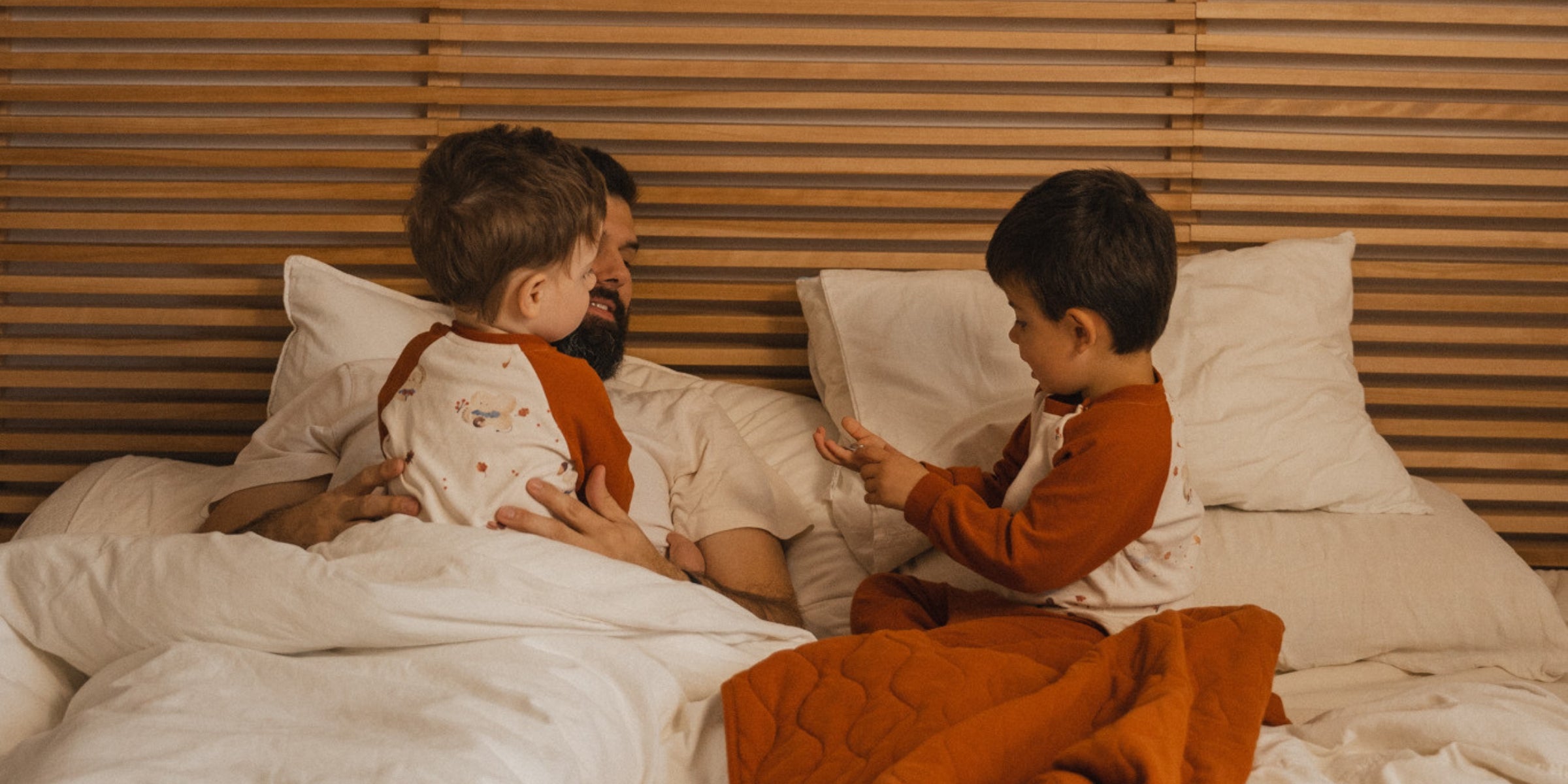 papa playing with two toddler boys on the bed