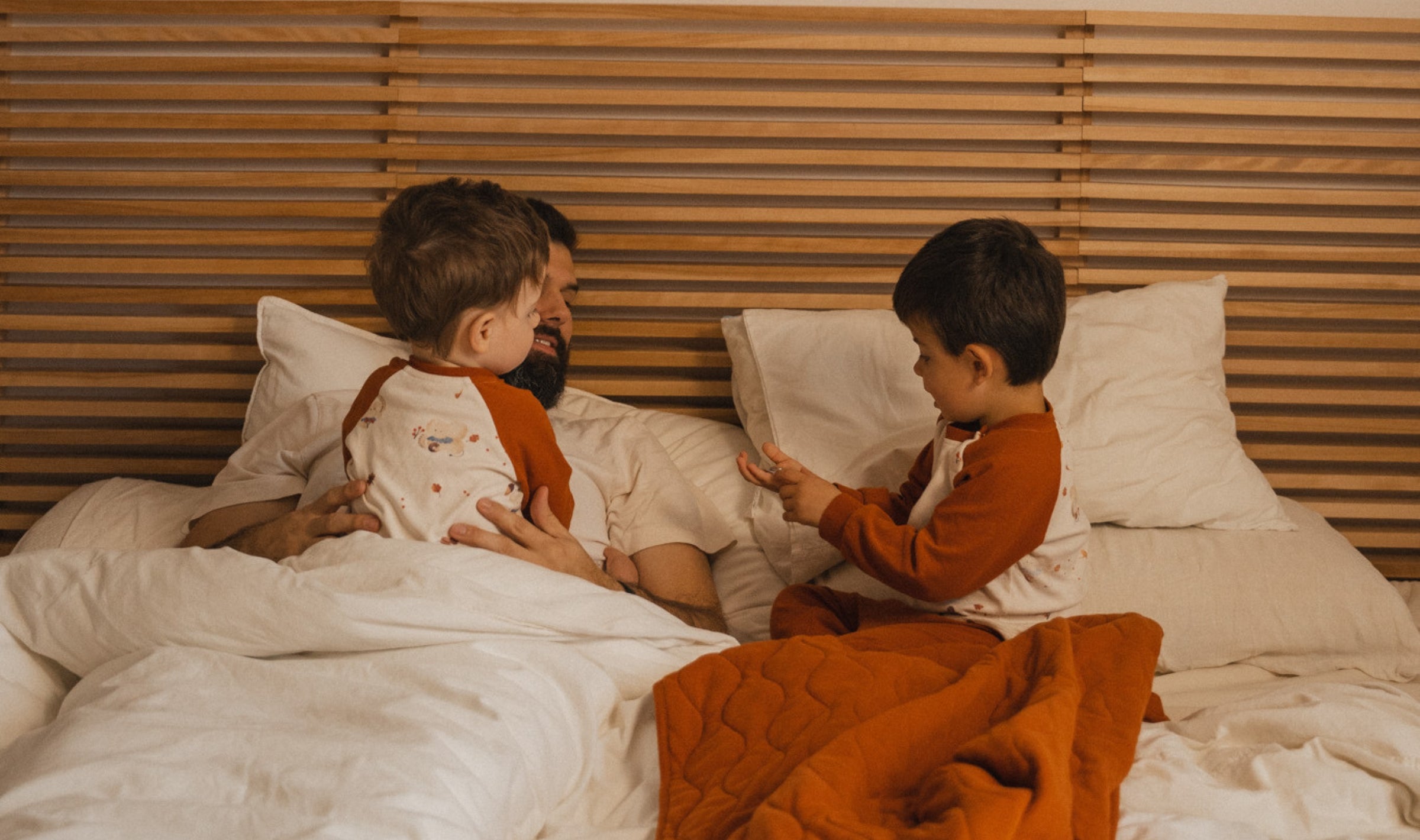 papa playing with two toddler boys on the bed