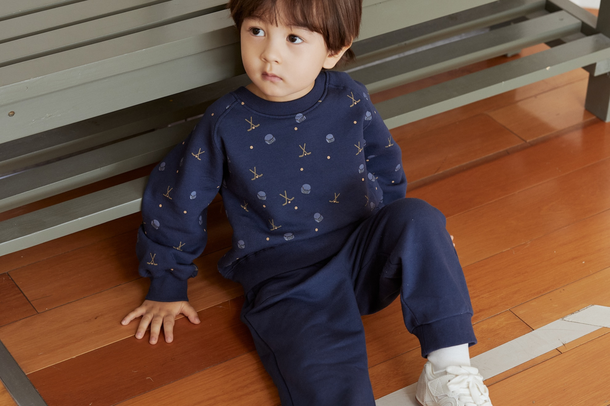 Child wearing a navy blue outfit with anchor pattern sitting on a wooden floor.