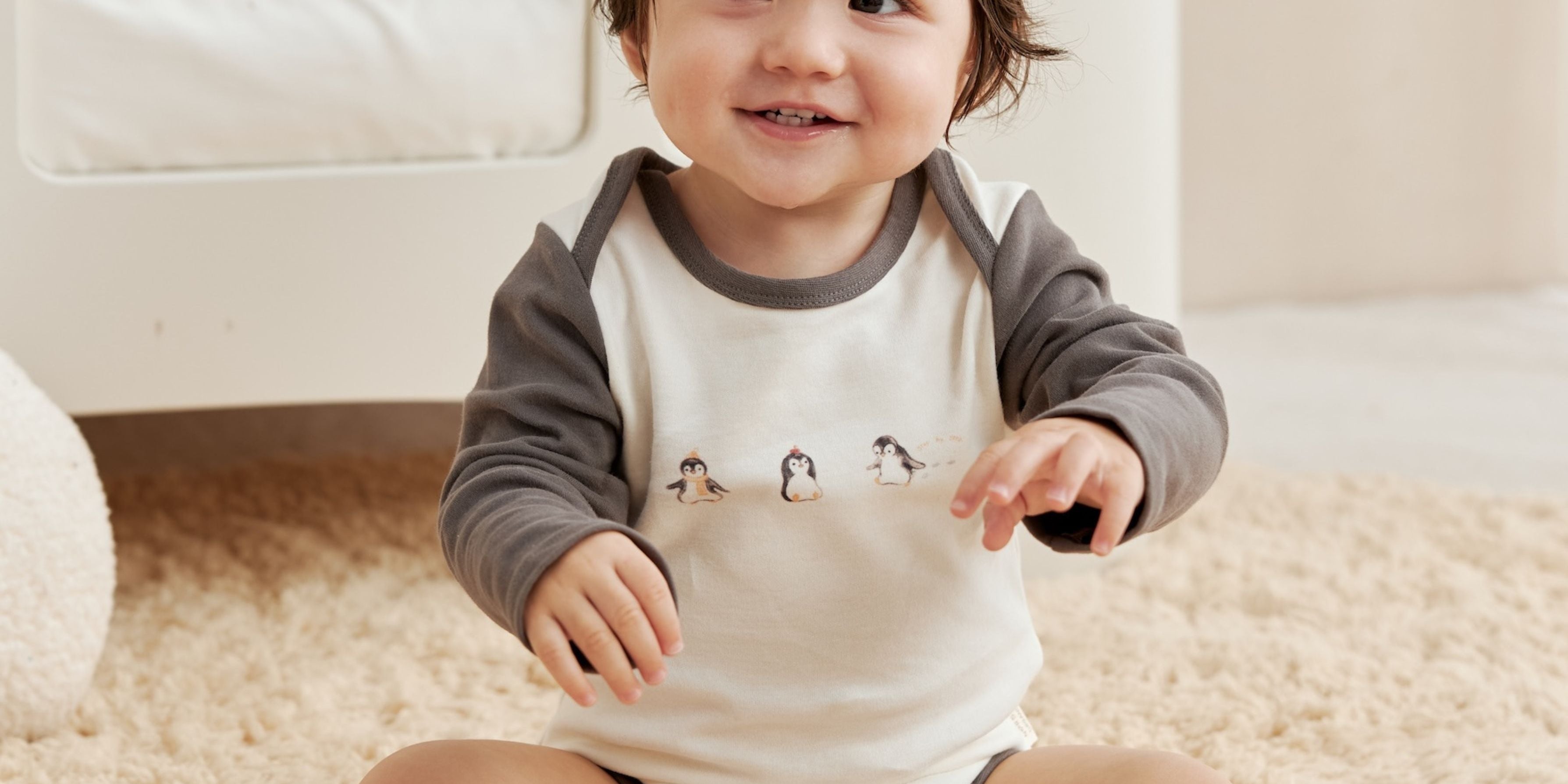Child wearing a onesie with penguin design sitting on a carpeted floor.