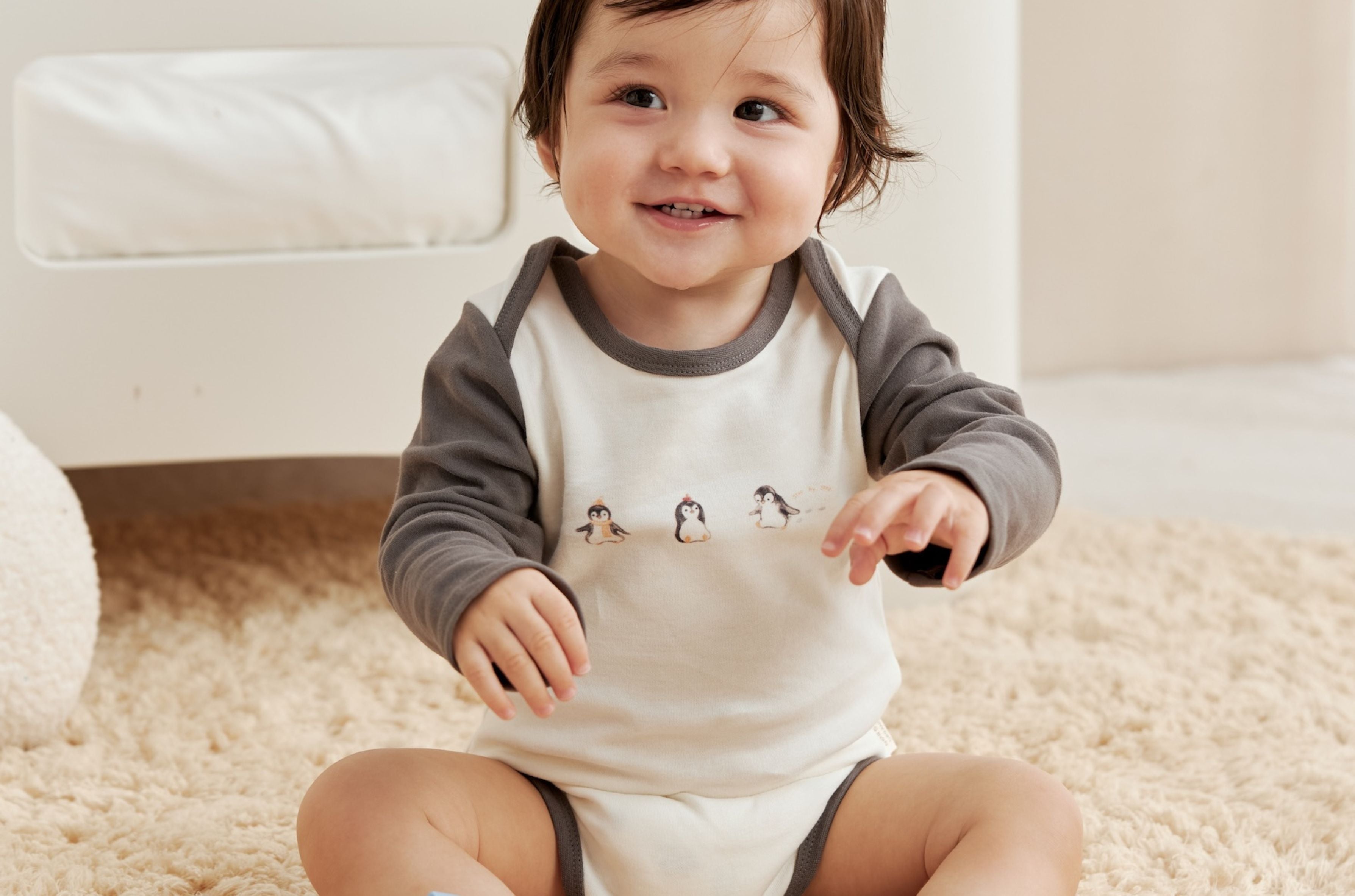 Child wearing a onesie with penguin design sitting on a carpeted floor.