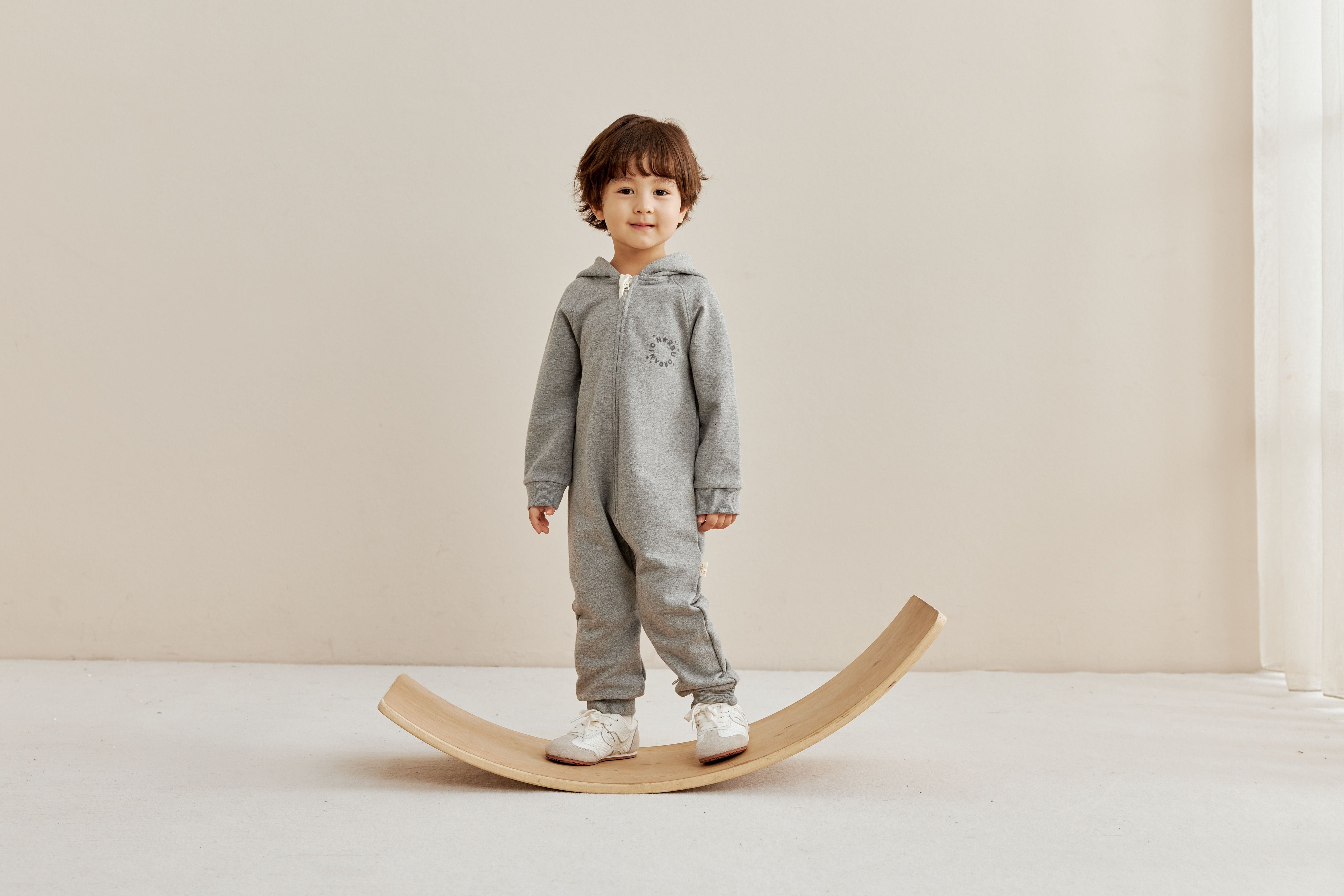 toddler boy in grey bodysuit standing on a borad in a warm room