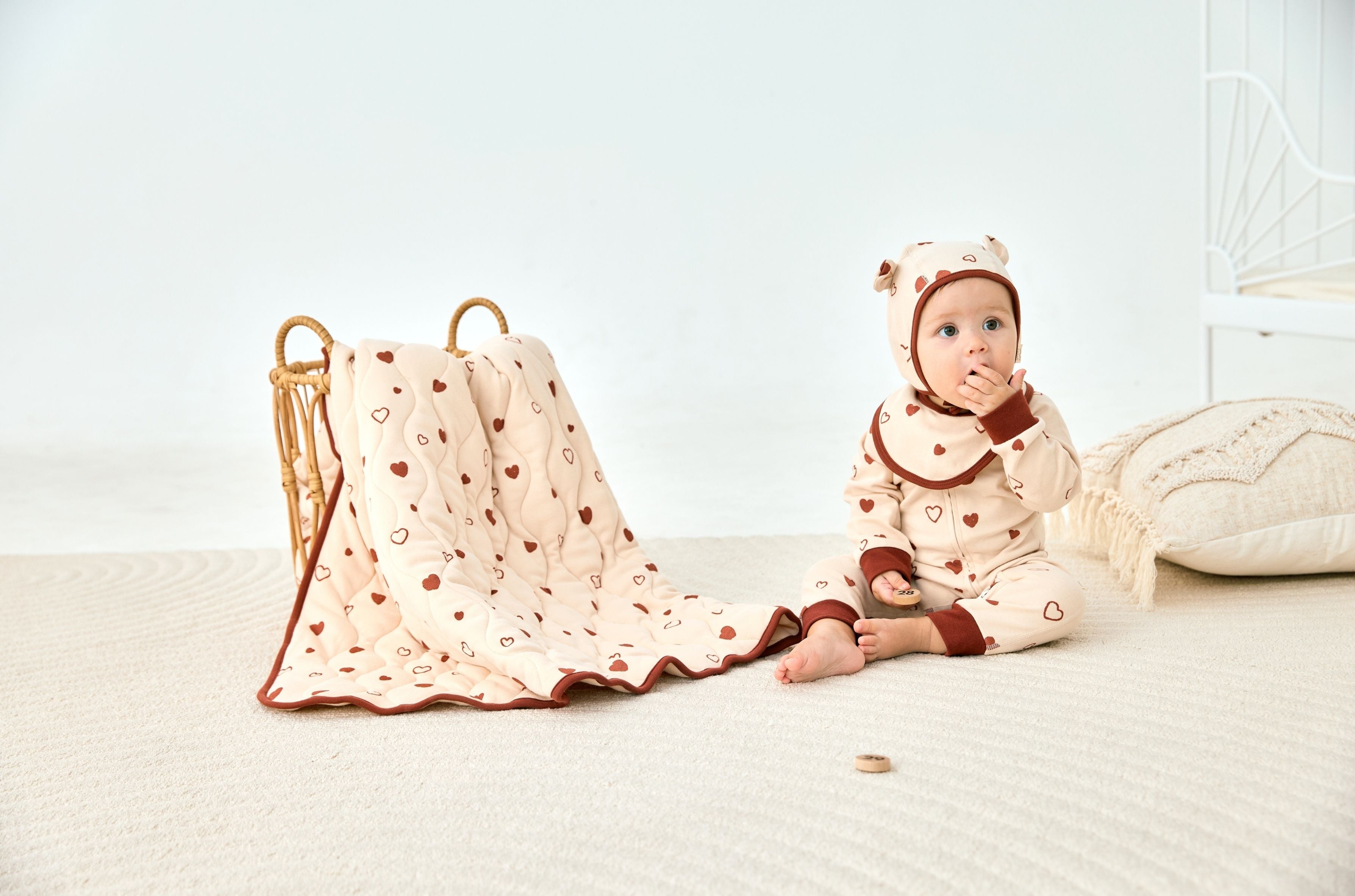 Child in navy outfit sitting on a beige rug with a blue blanket and white sofa in the background