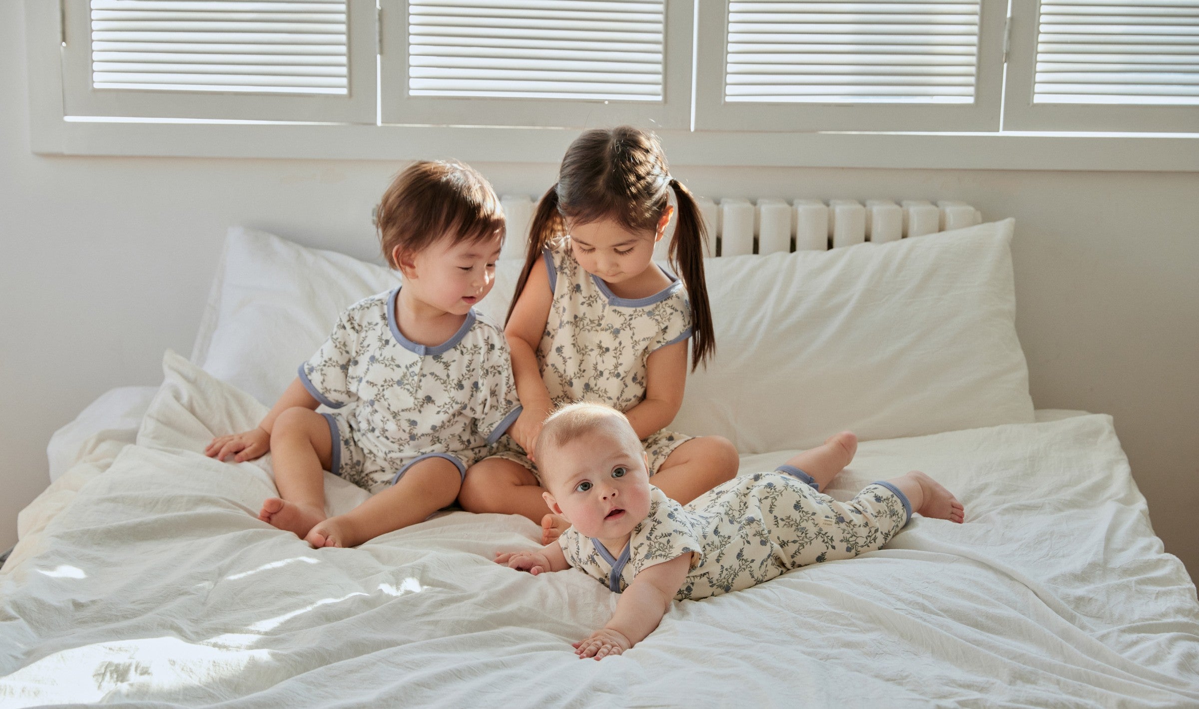 one toddler boy and his toddler sister are playing with a baby on the bed