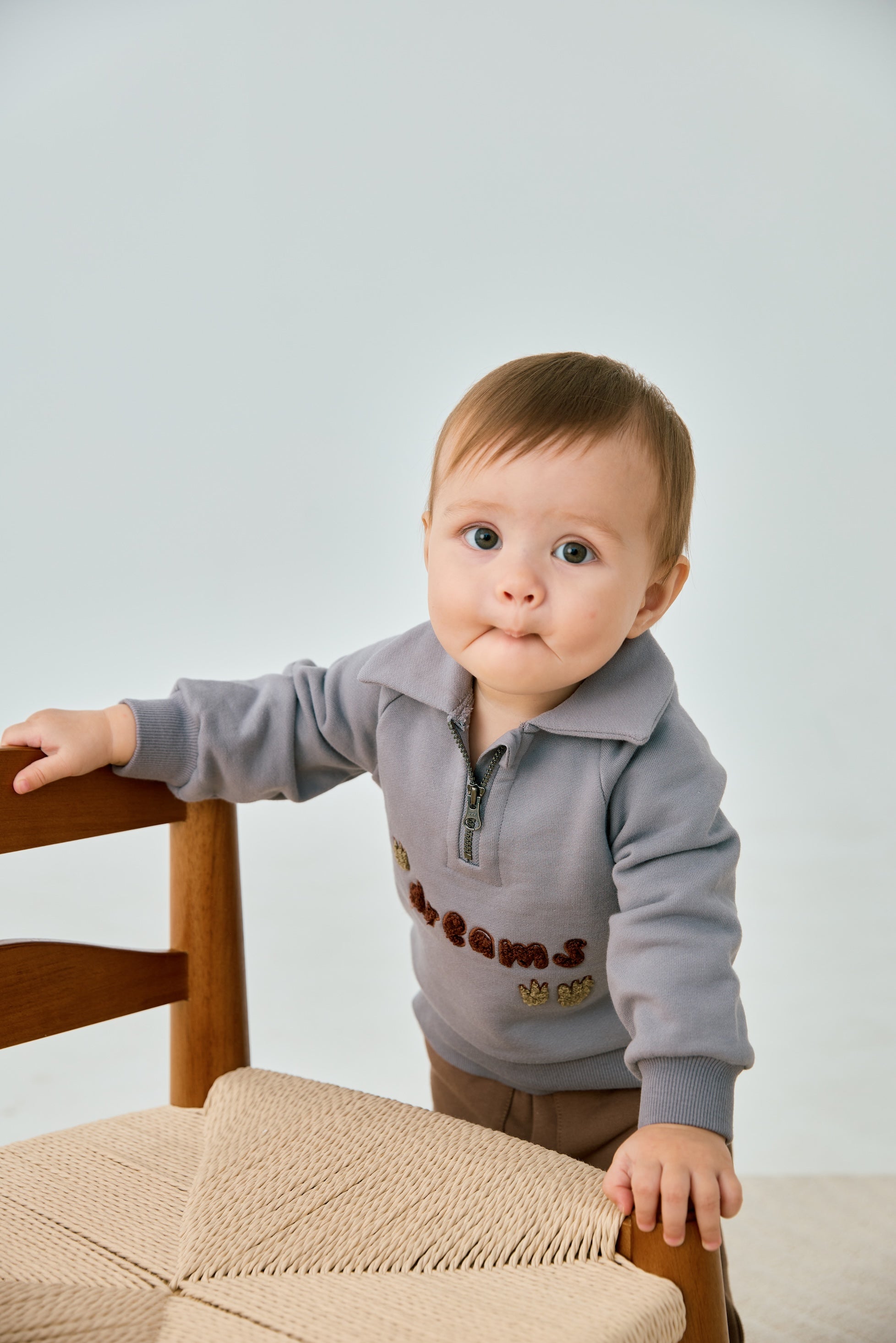 baby standing beside chair and wearing Toddler Organic Fleece Zip-up Sweatshirt-Dreams