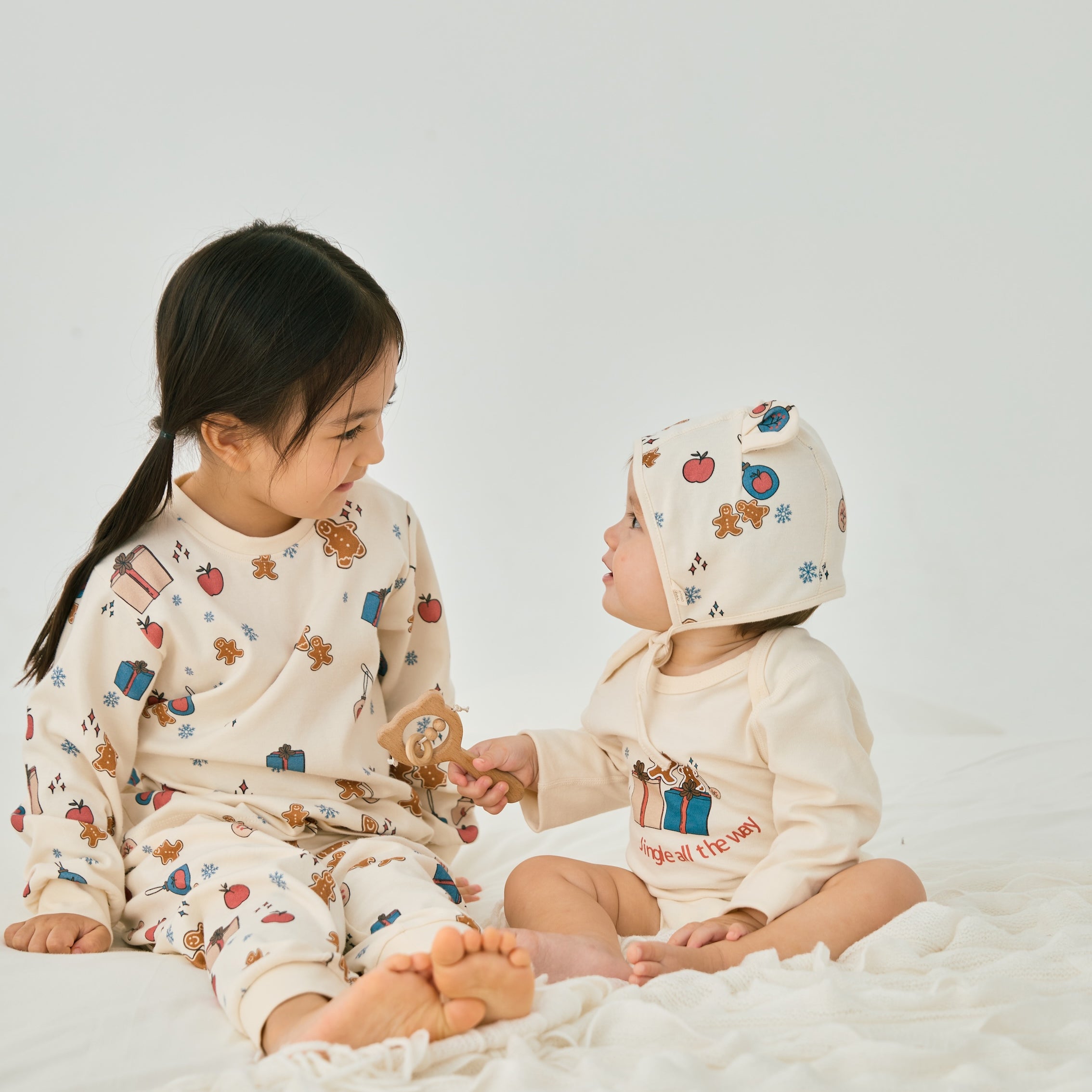 baby girl wearing Organic Toddler Pajama Set-Holiday Joy and watching a baby