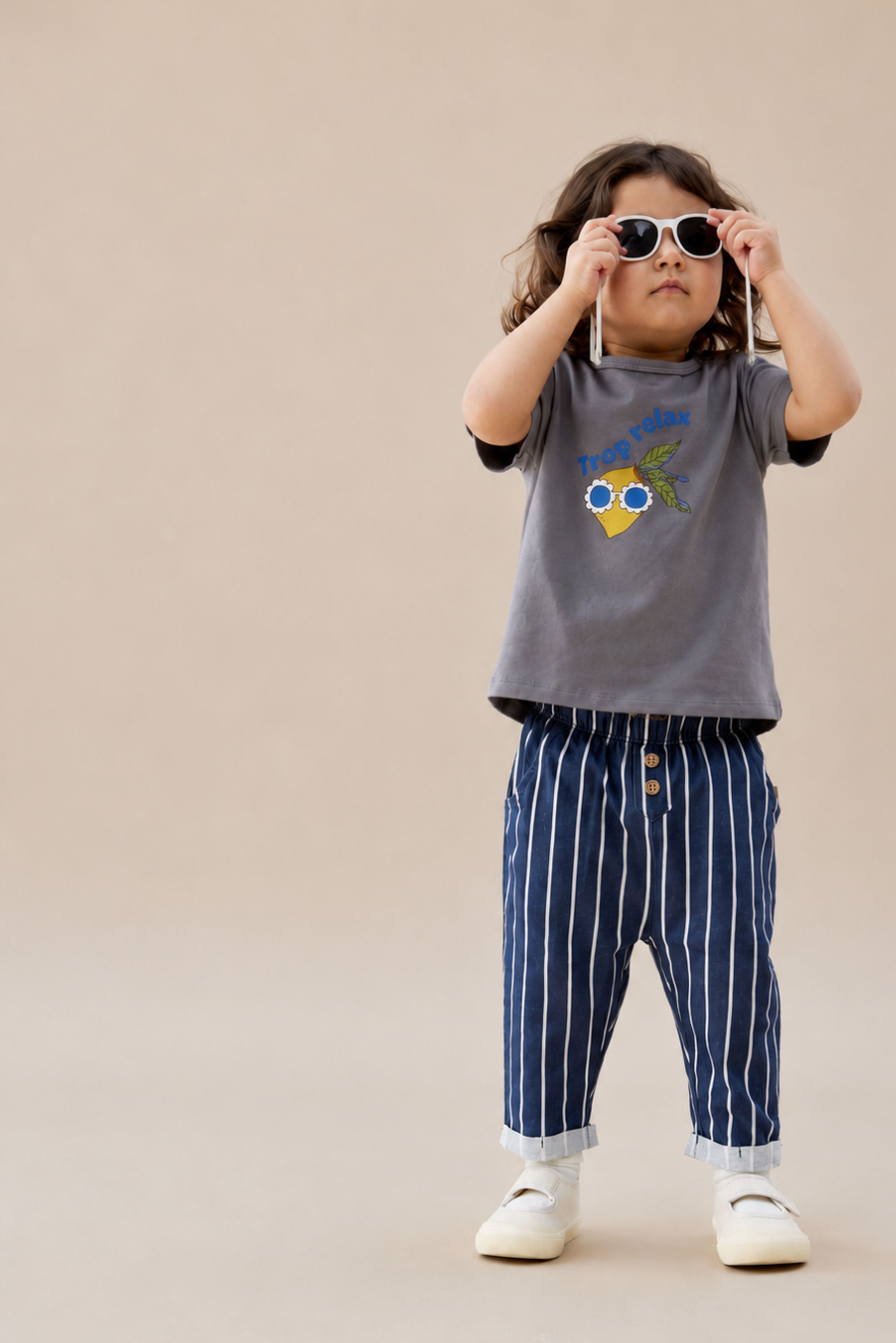 Child wearing a gray t-shirt with a colorful design and blue striped pants on a beige background