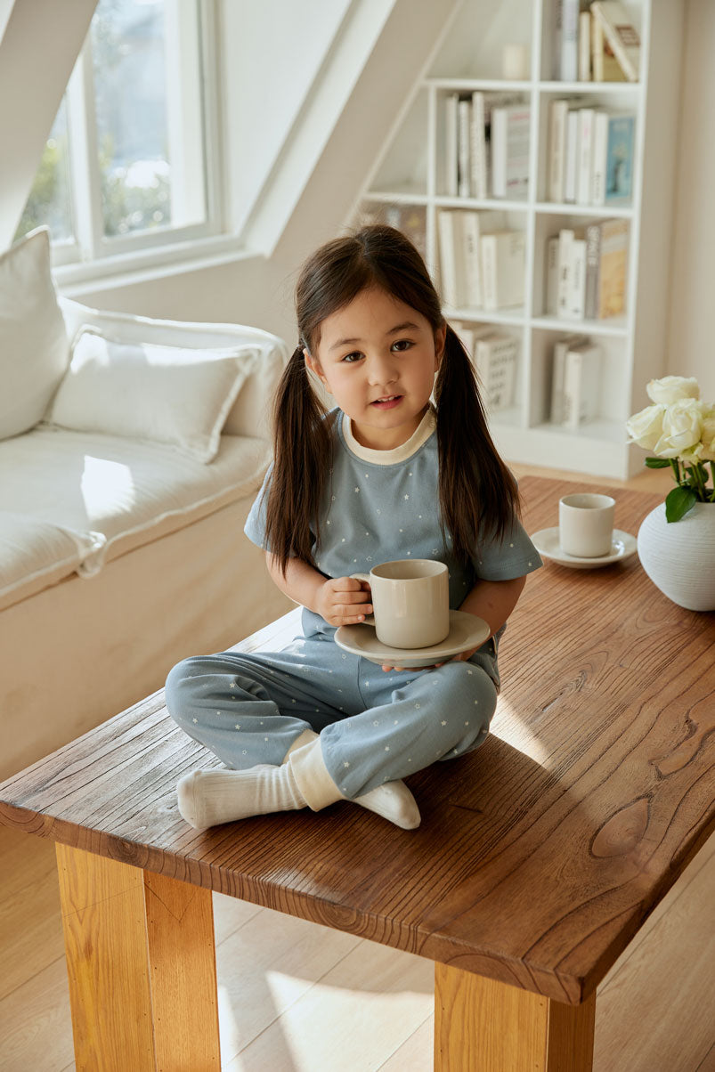 baby girl sitting and table and holding a cup of tea