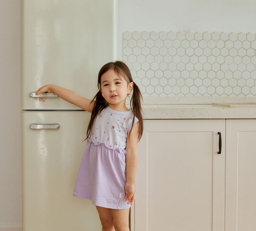 baby standing beside fridge and smiiling at you