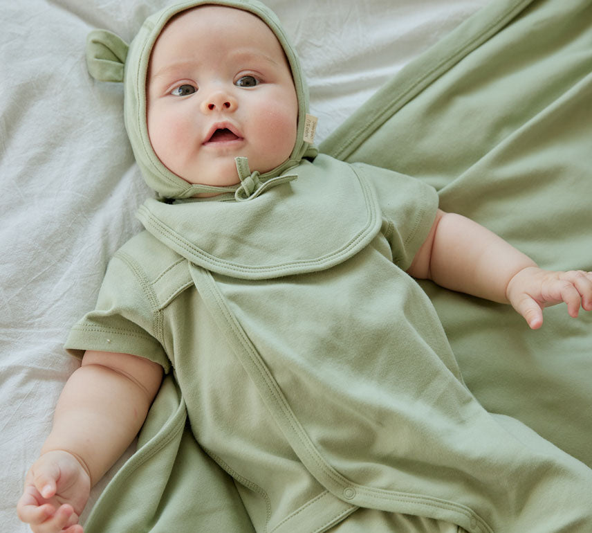 baby is laying on the bed and wearing Baby Organic Kimono Sleeper-Grey Green