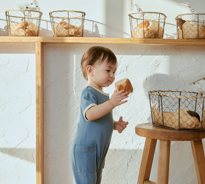 baby holding a bread and stand infront of a chair