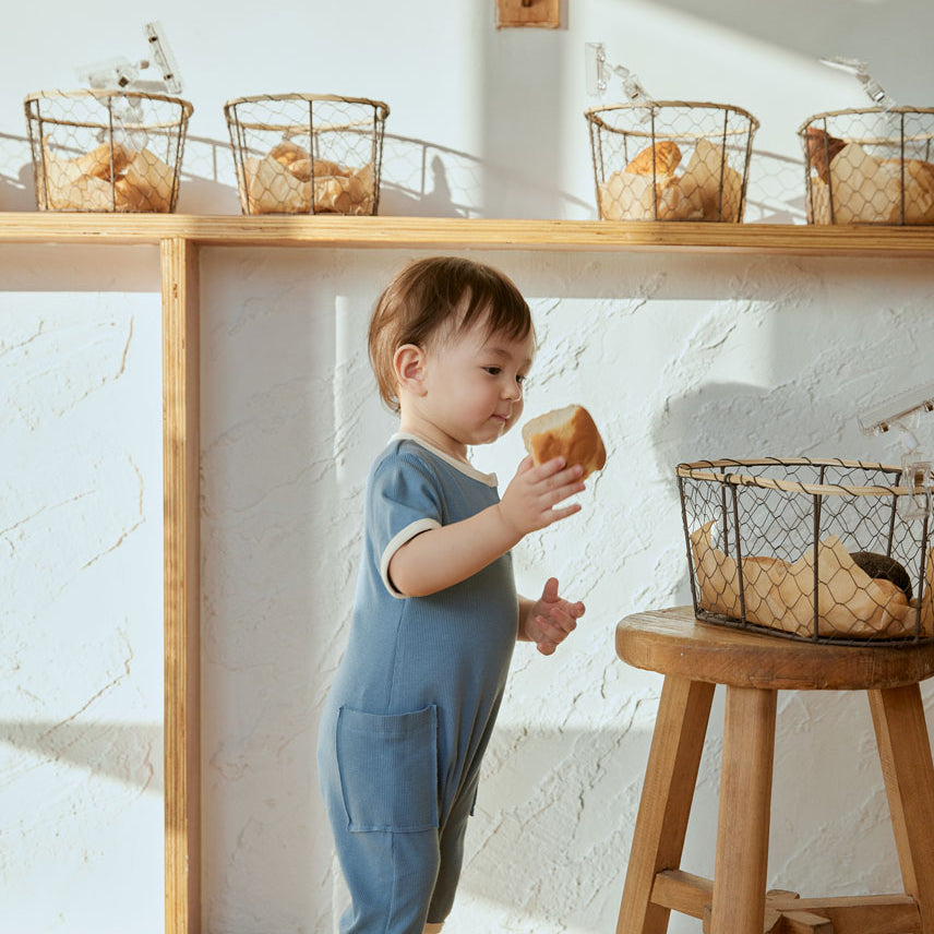 baby holding a bread and stand infront of a chair