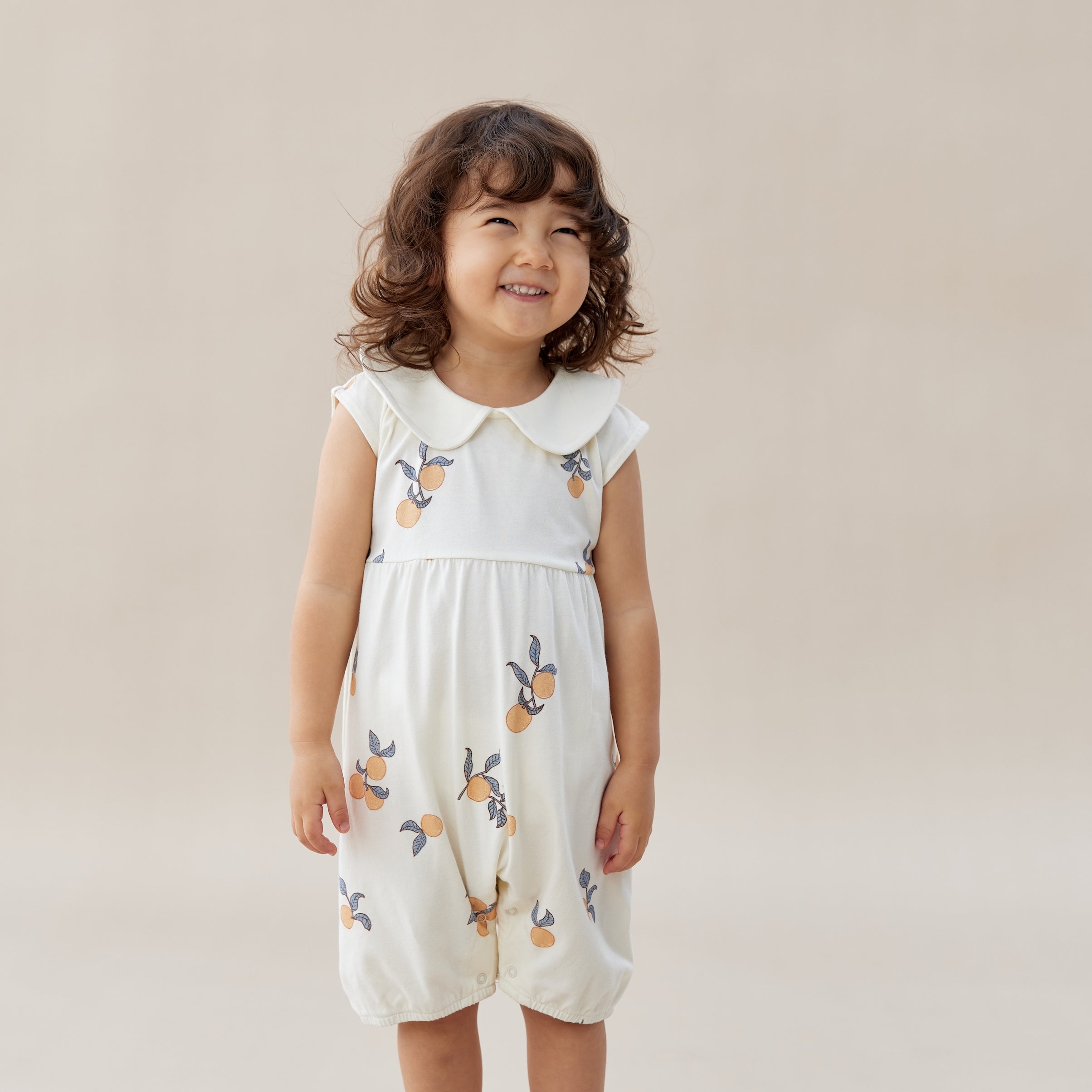 Child wearing a white romper with floral patterns on a beige background