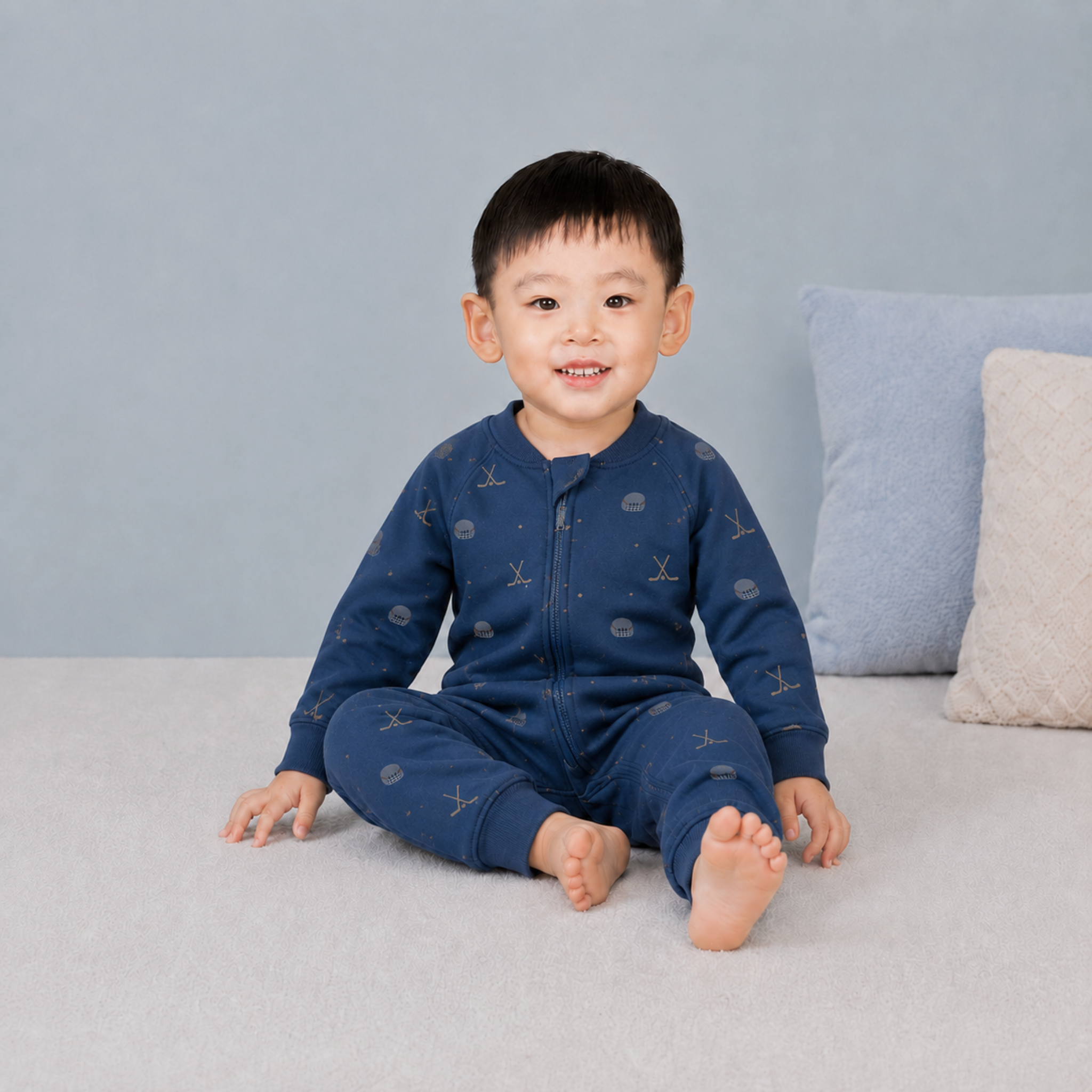 Child wearing a blue bodysuit with hockey patterns on a gray couch.
