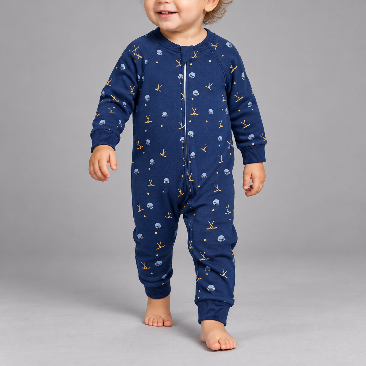 A baby wearing a navy blue one-piece romper with a gold and white anchor pattern, standing against a solid gray studio background.
