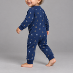 A baby wearing a navy blue long-sleeve jumpsuit with a gold and white space-themed print of planets, stars, and rockets, walking against a solid gray studio background.