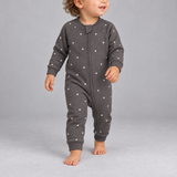 A baby wearing a dark gray long-sleeve footless sleeper with a white star pattern, walking barefoot against a solid gray studio background.