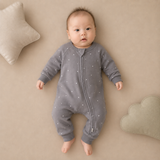 Baby in a gray bodysuit with white stars lying on a beige surface.