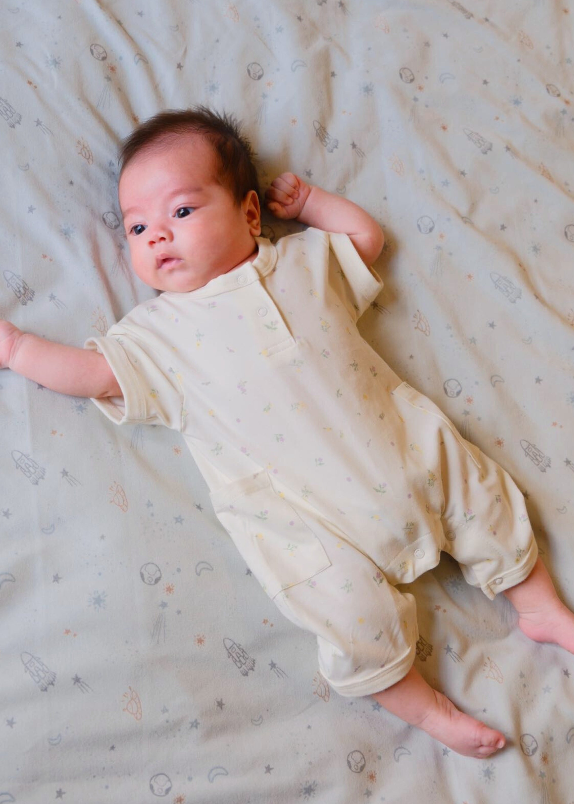 1. A cute baby in a floral organic bamboo romper, peacefully laying on a cozy bed with a soft blanket.
