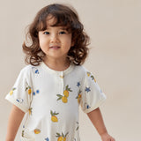 Child wearing a white romper with fruit patterns on a plain background