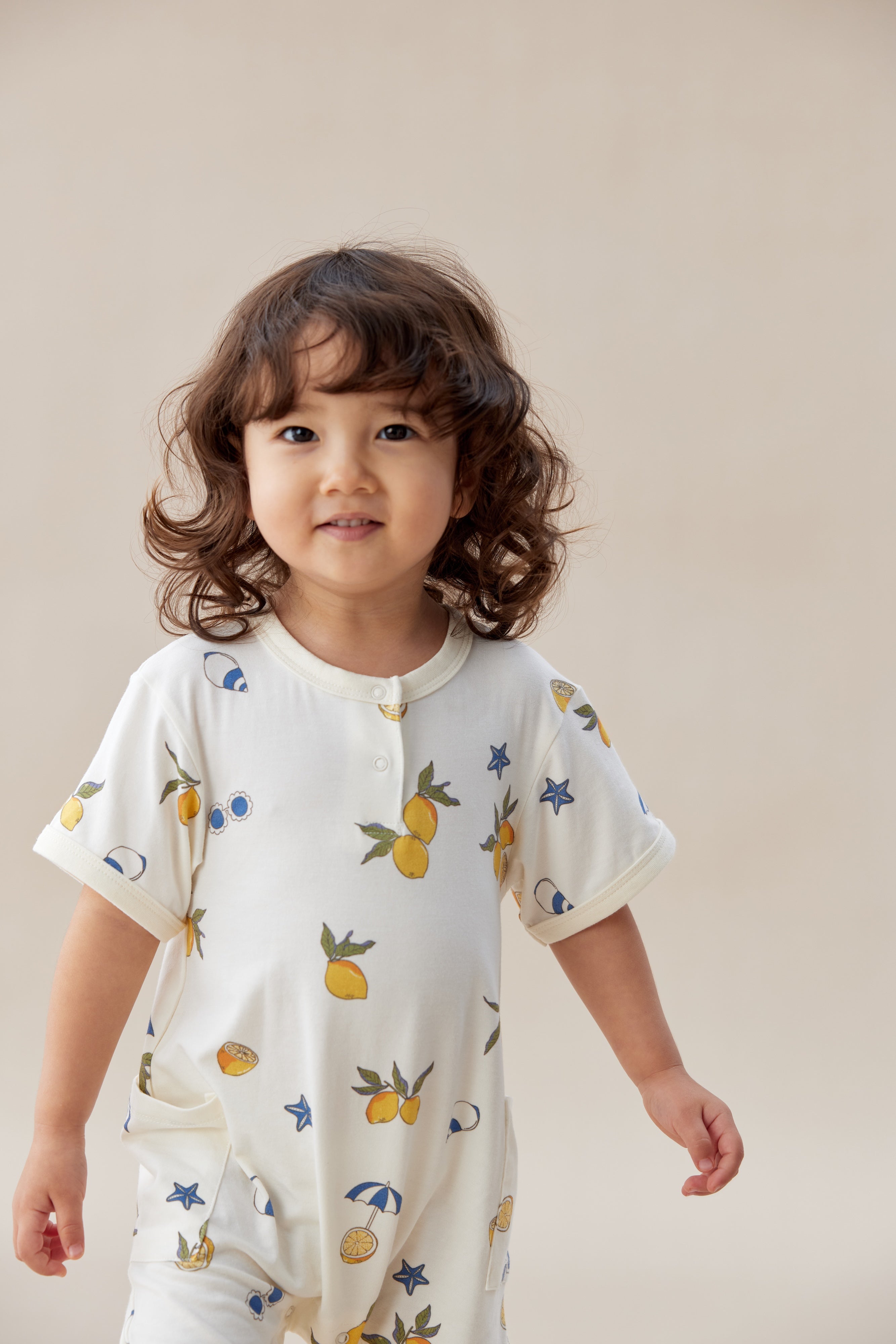 Child wearing a white romper with fruit patterns on a plain background