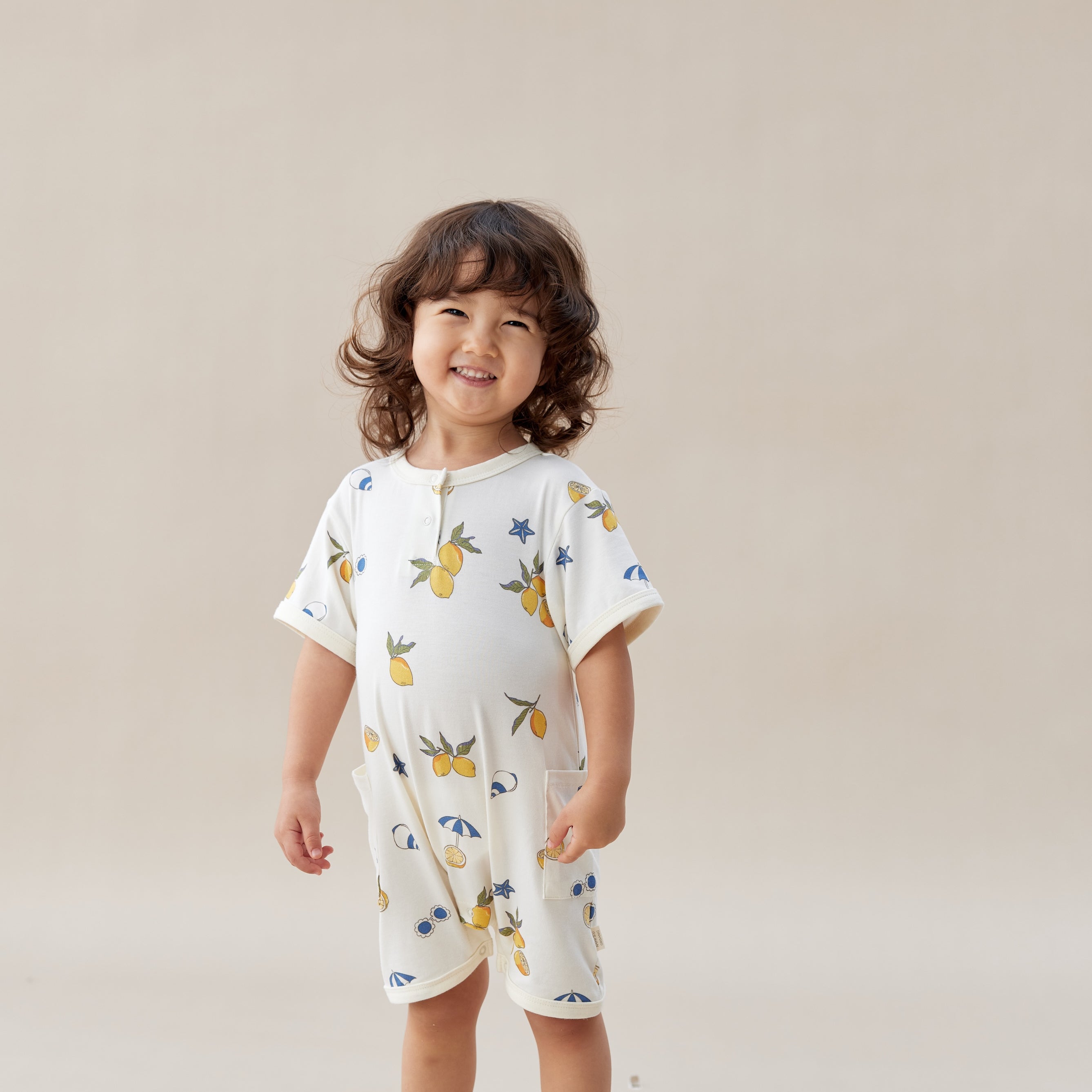 Child wearing a lemon romper with colorful patterns on a beige background