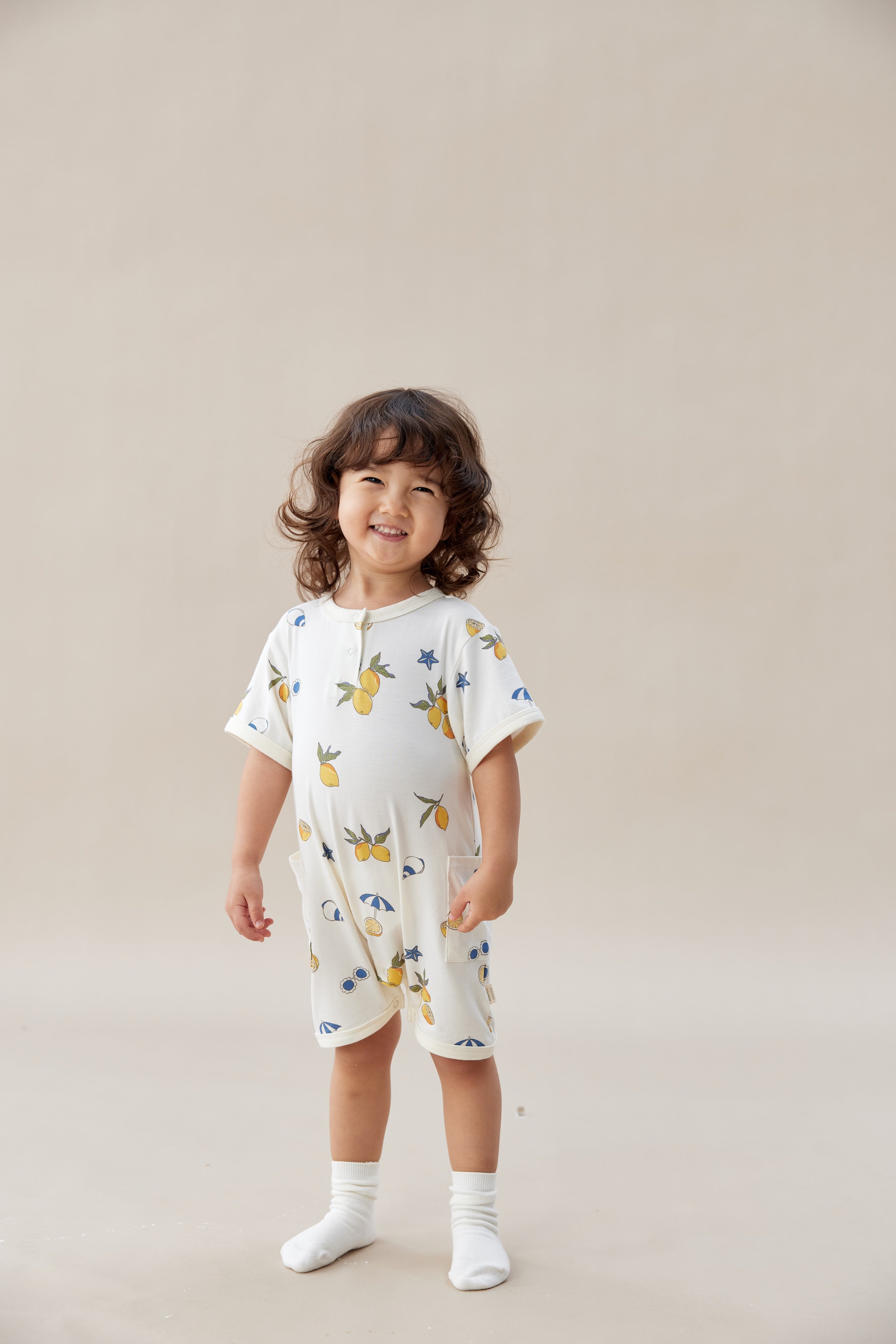 Child wearing a lemon romper with colorful patterns on a beige background