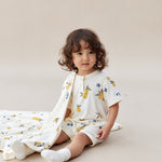 Child wearing a lemon romper with colorful patterns sitting on a beige surface.