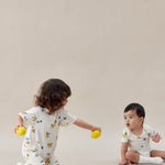 Two children in white onesies with colorful patterns playing on a beige surface.