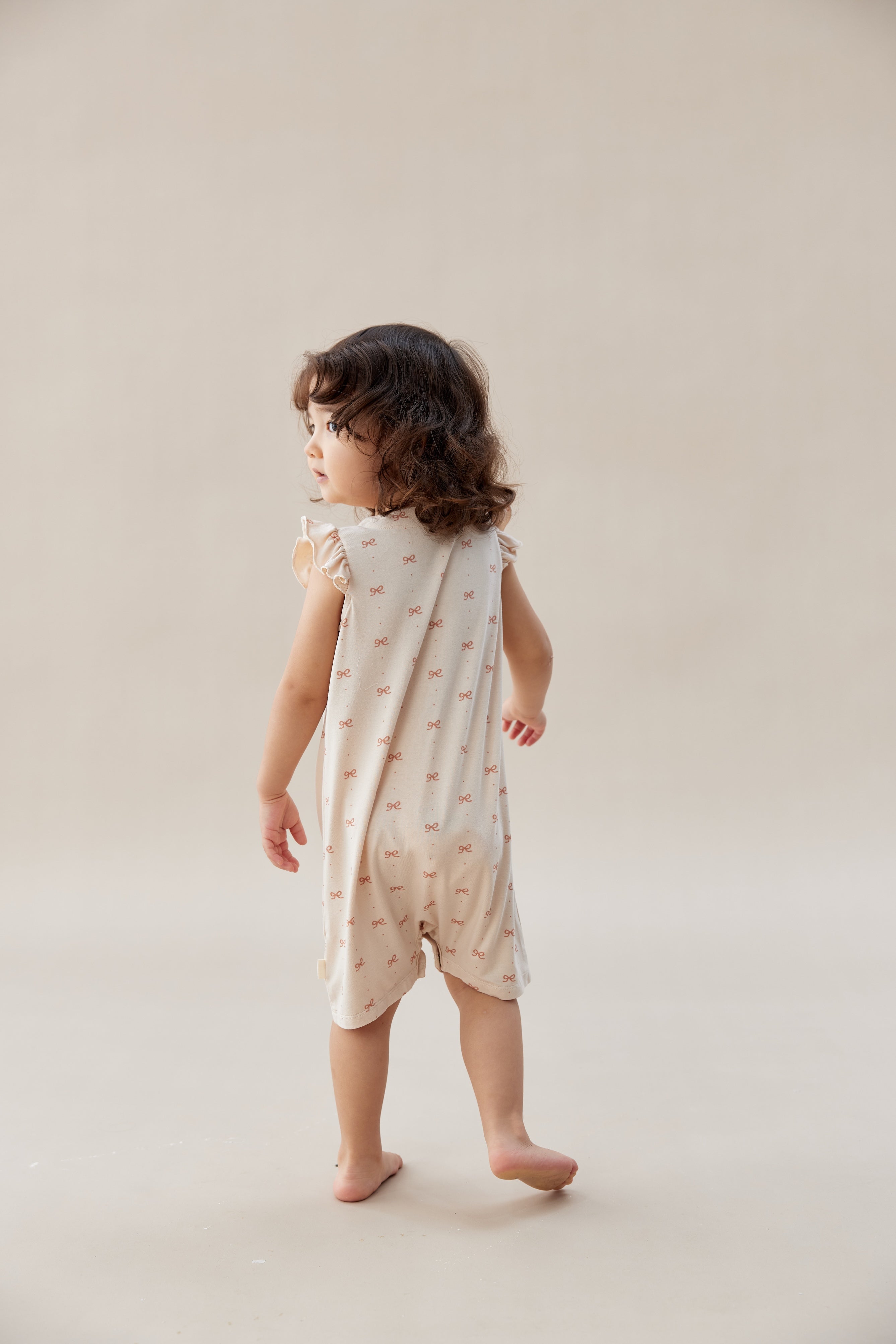 Child wearing a light-colored dress with a subtle pattern on a plain background