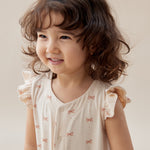 Young girl wearing a light-colored dress with ruffled sleeves against a plain background