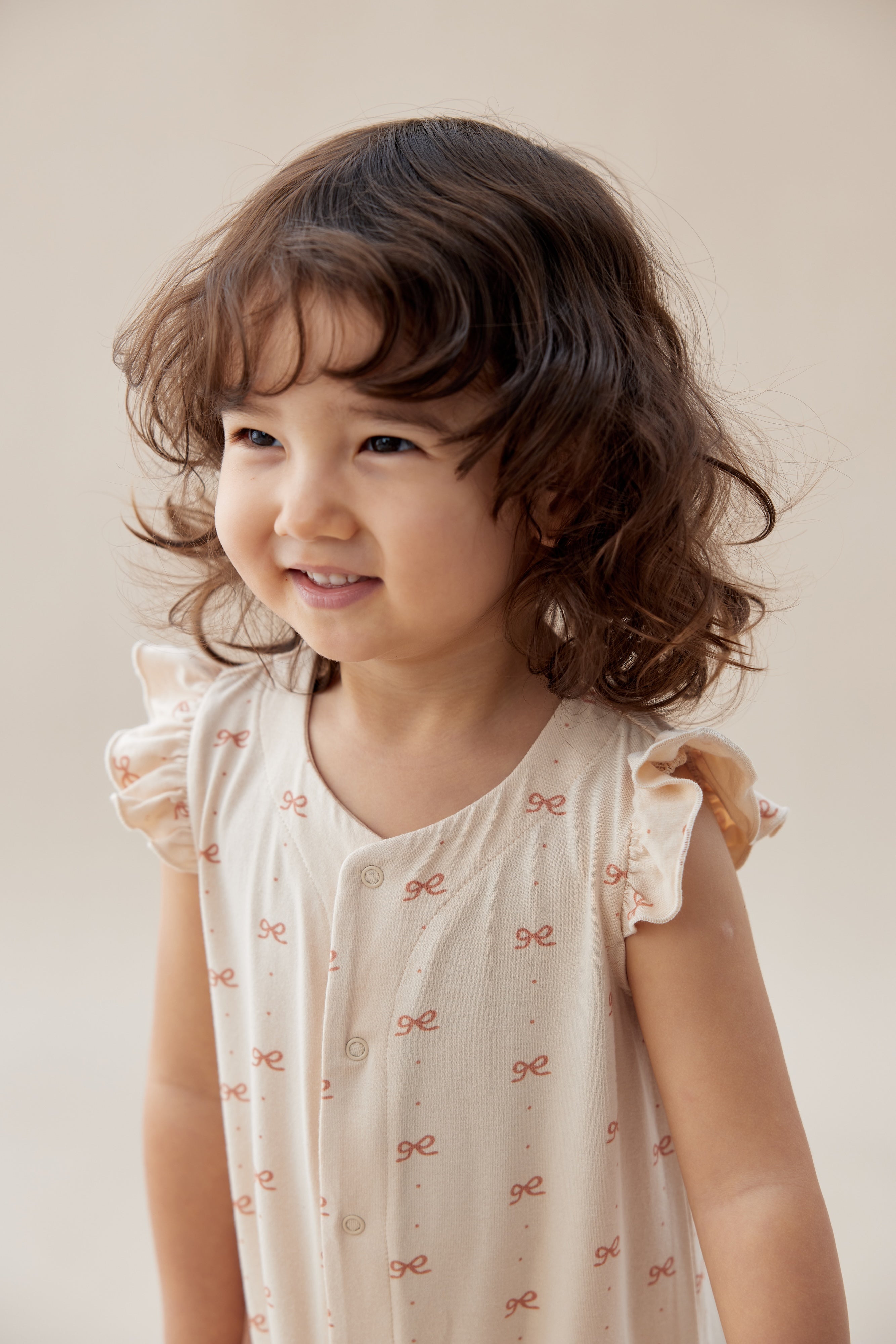 Young girl wearing a light-colored dress with ruffled sleeves against a plain background