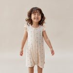 Child wearing a light-colored dress with a subtle pattern on a plain background