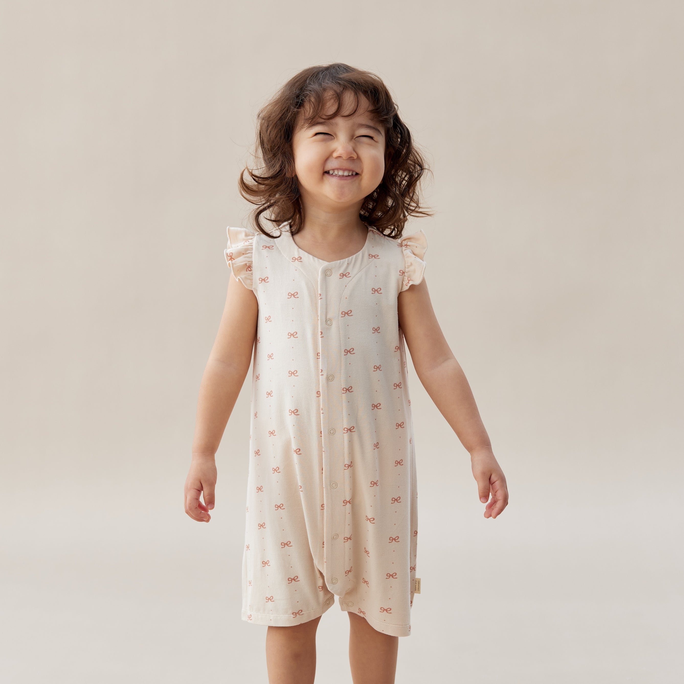 Child wearing a light-colored dress with a subtle pattern on a plain background