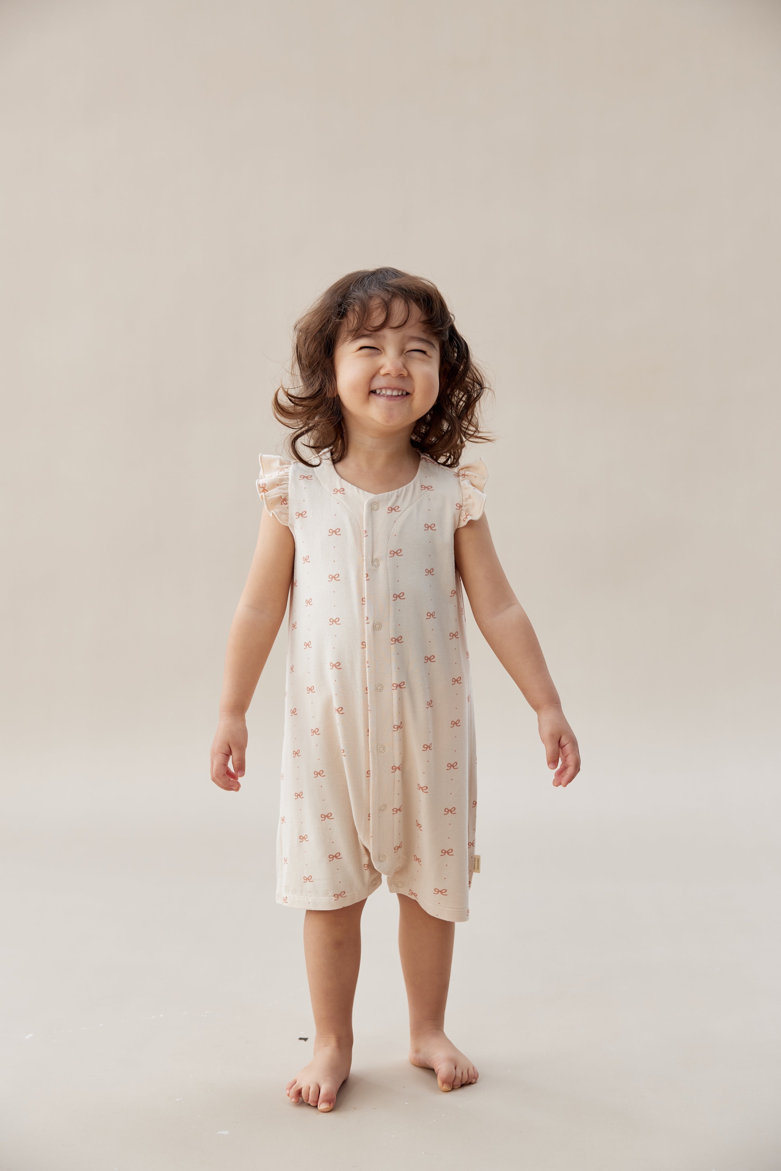 Child wearing a light-colored dress with a subtle pattern on a plain background