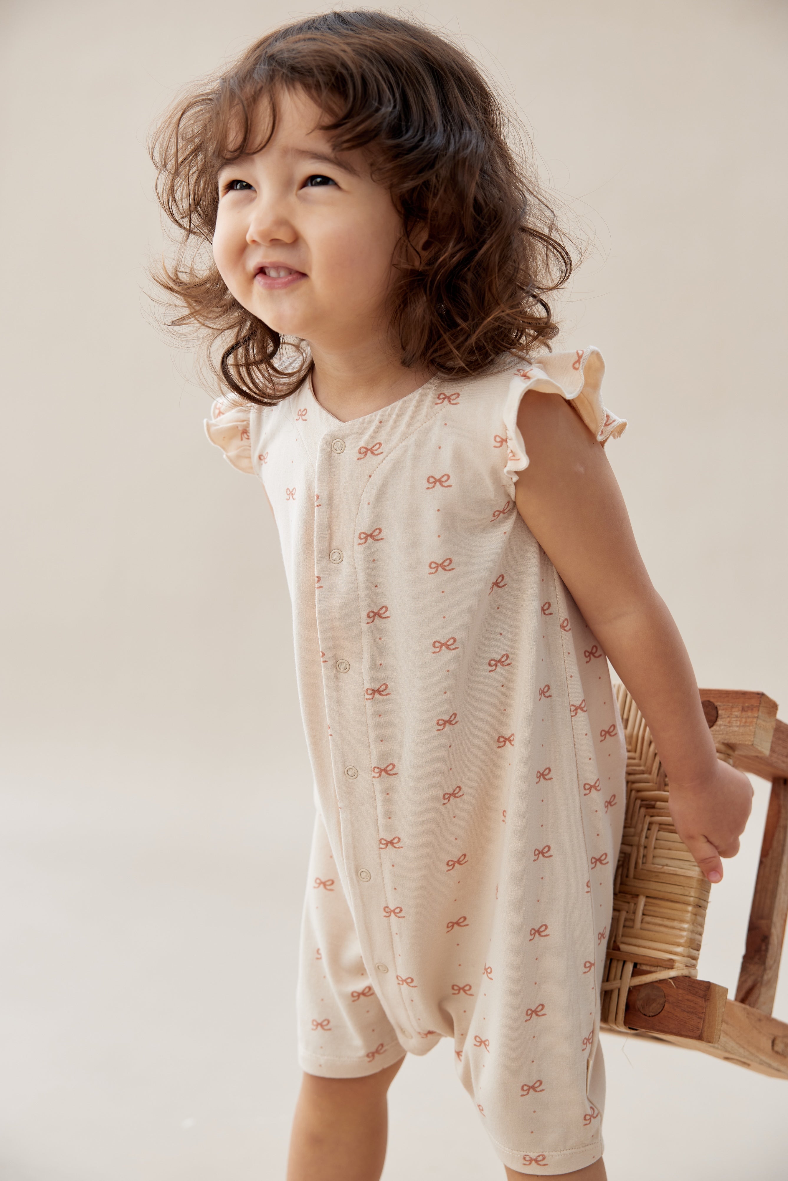 Child wearing a white dress with small patterns, holding a woven basket against a plain background
