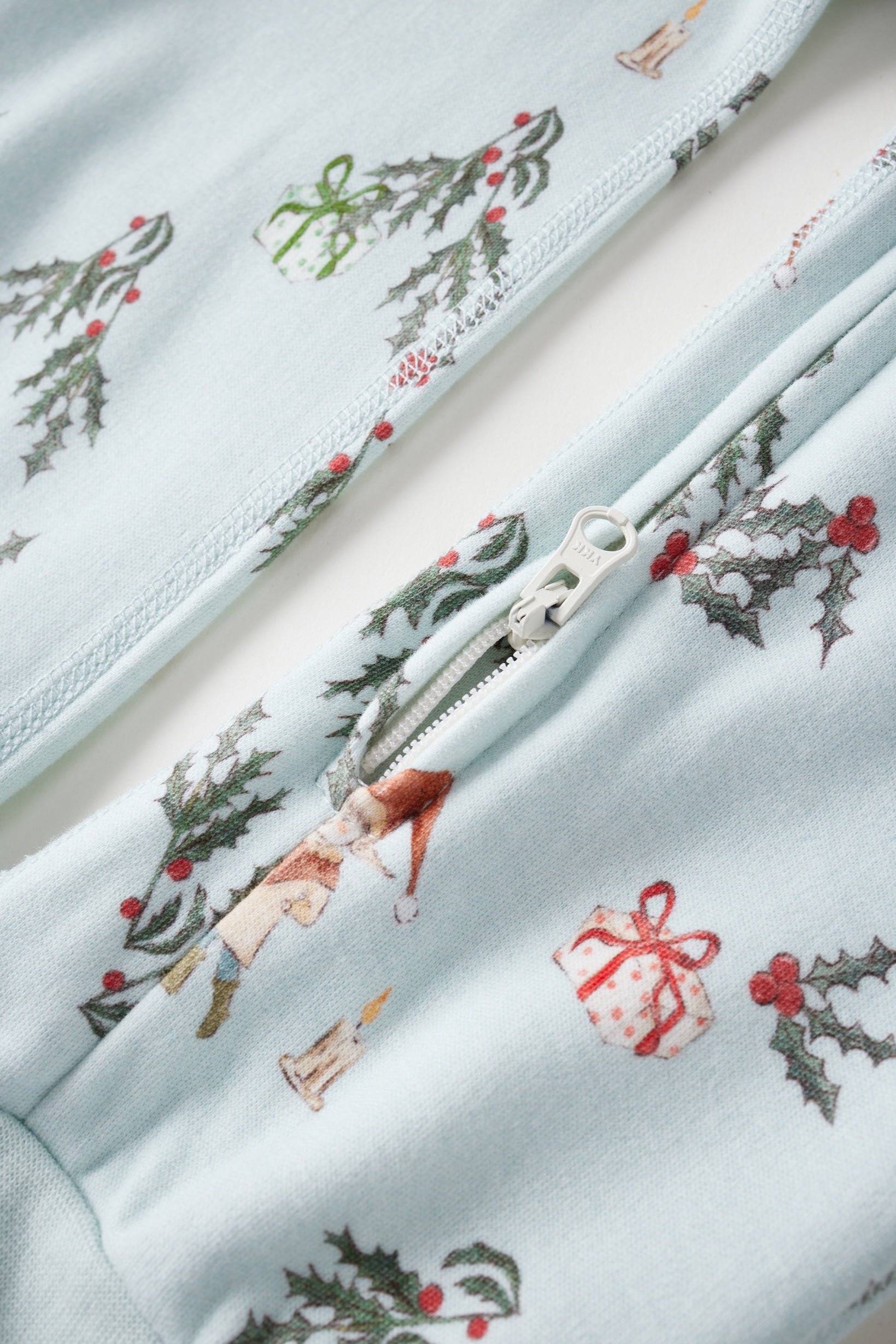 Close-up of a fabric with Christmas-themed designs including holly leaves, ribbons, and a snowman on a light blue background.