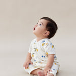 Baby sitting on a beige surface wearing a white outfit with colorful patterns.