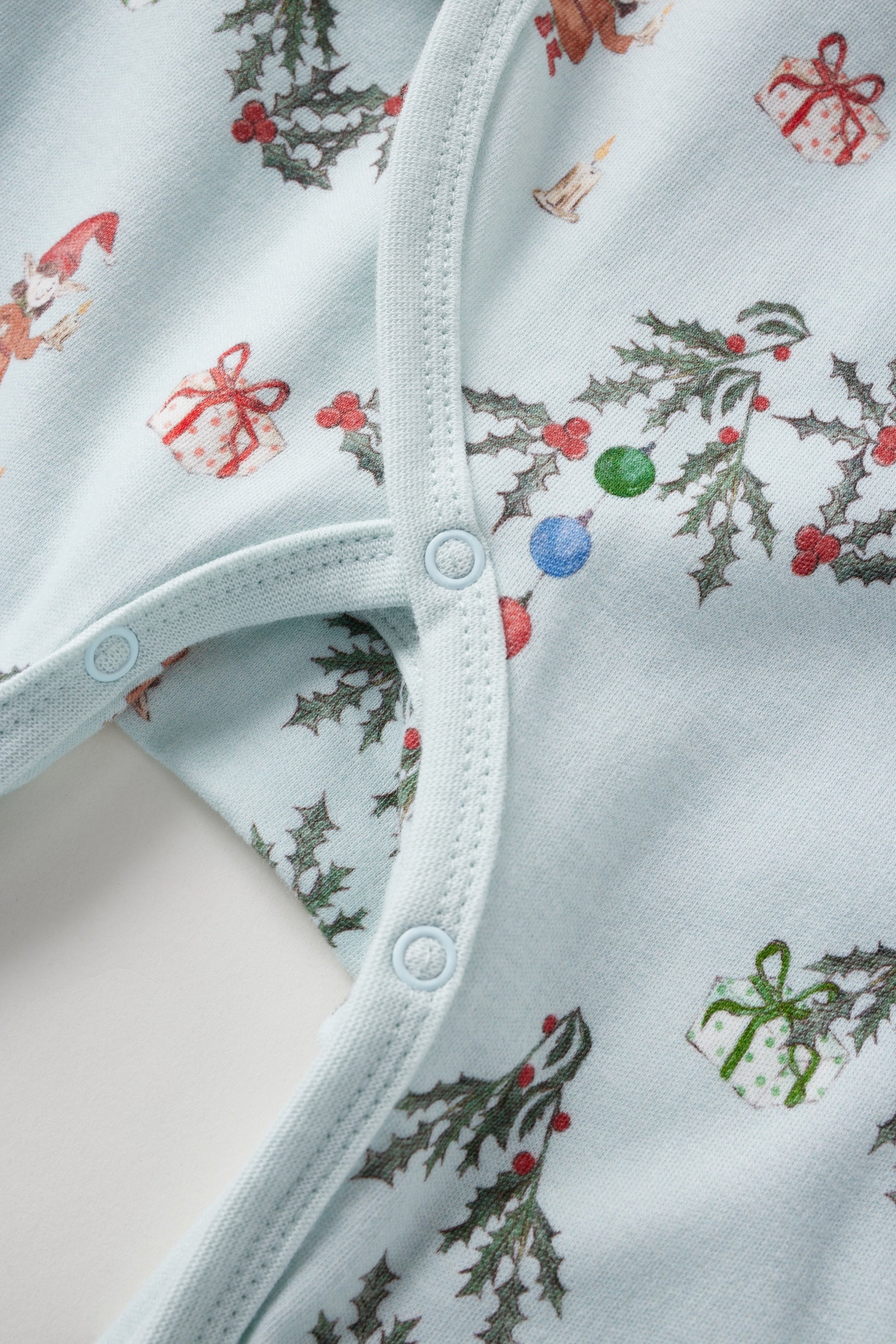 Close-up of a baby sleeper with Christmas-themed print on a light blue background