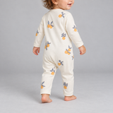 A baby wearing a cream-colored long-sleeve footless jumpsuit with a yellow-orange fruit print, shown from the back against a neutral gray background.