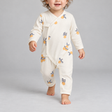 A baby wearing a cream-colored long-sleeve footless sleeper with a yellow and gray fruit print, walking against a light gray background.