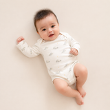 A baby lying on a light beige background wearing a long-sleeve white bodysuit with a small gray cloud pattern.