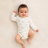 A baby lying on a light beige surface, wearing a long-sleeve white bodysuit with a small gray cloud pattern.