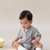 Baby in a gray outfit sitting on a beige surface with a white background