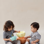 Two children playing with colorful bowls on a plain background