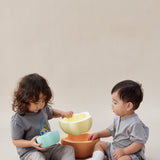 Two children playing with colorful bowls on a plain background