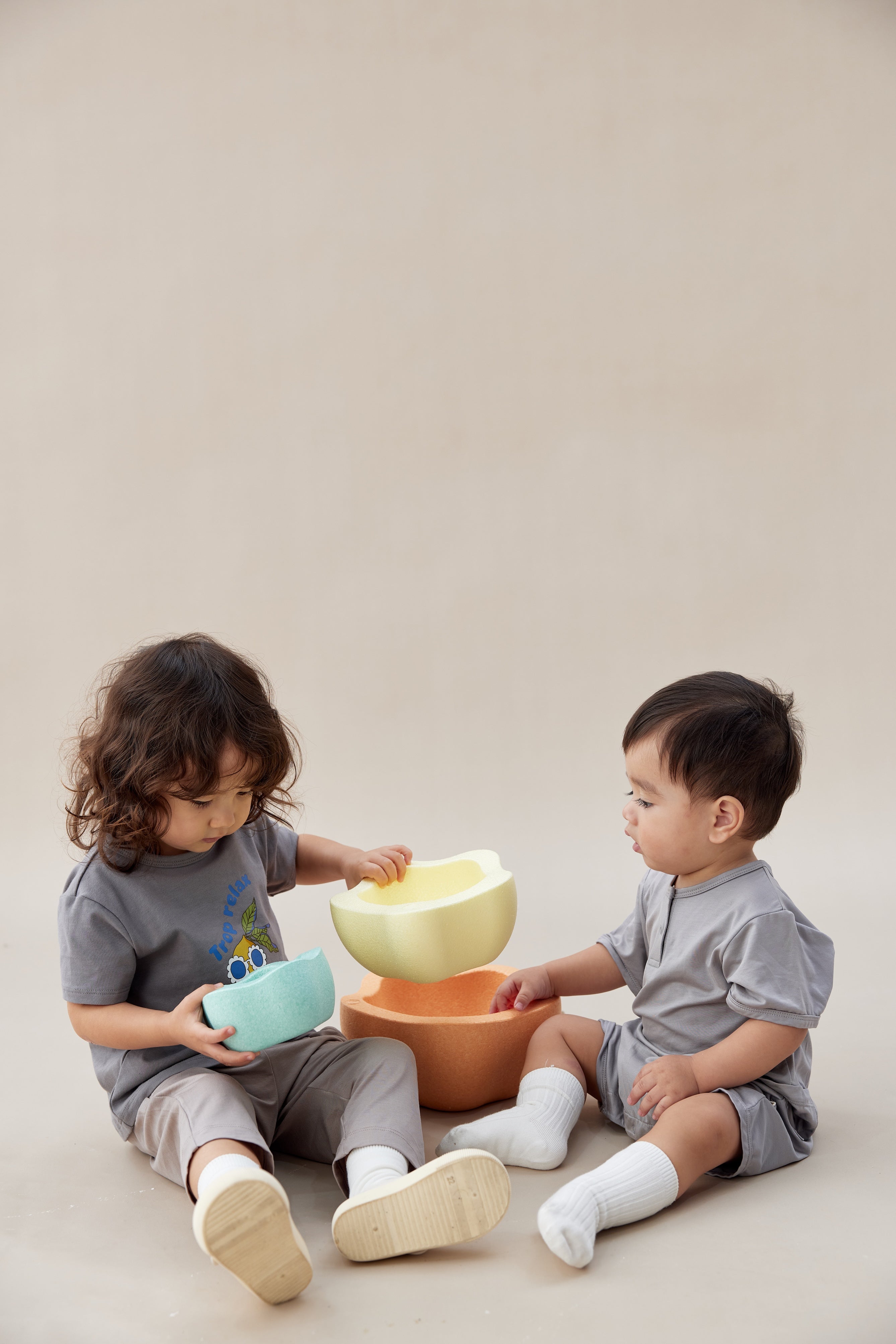 Two children playing with colorful bowls on a plain background