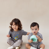 Two children in matching outfits sitting on a plain background