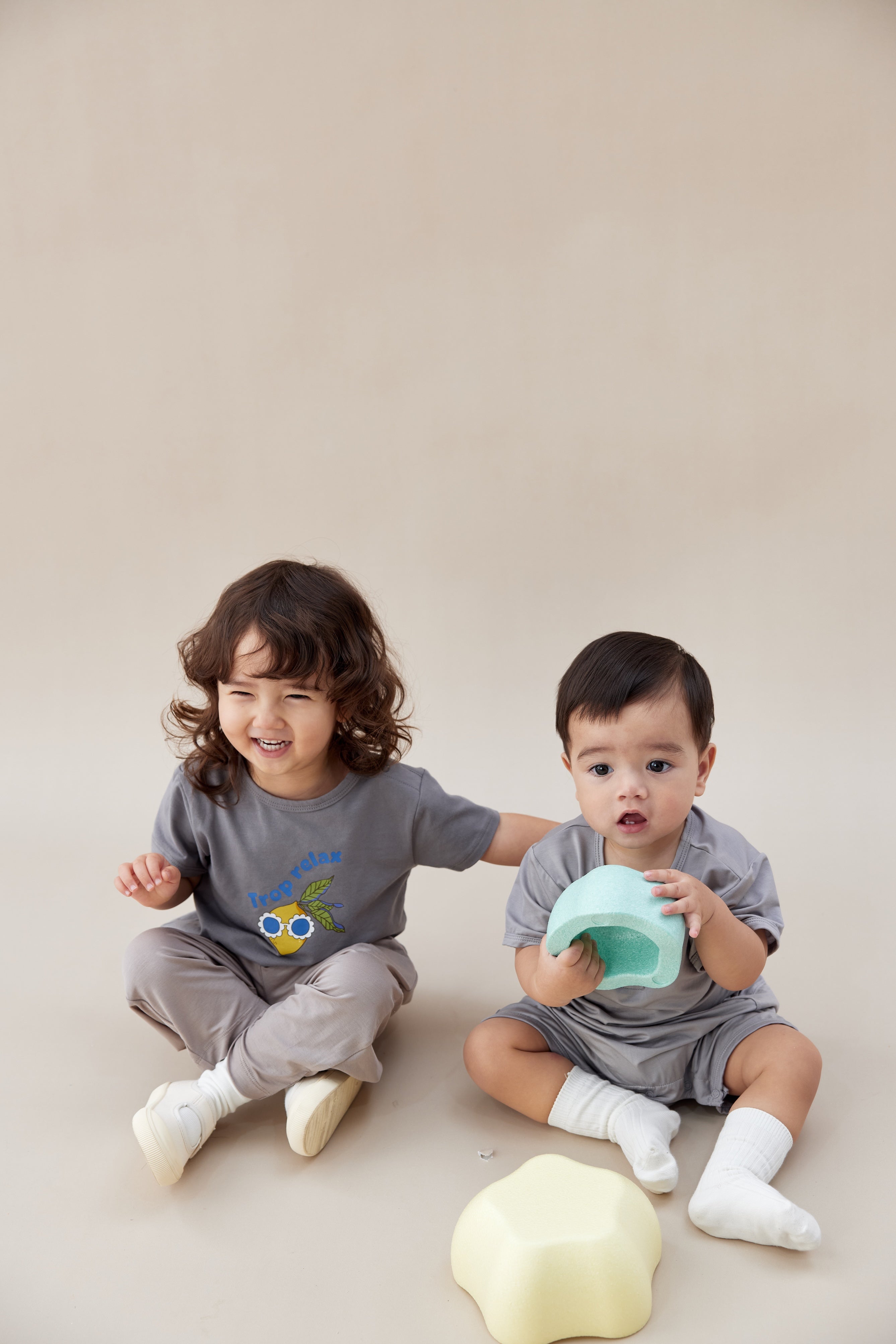Two children in matching outfits sitting on a plain background